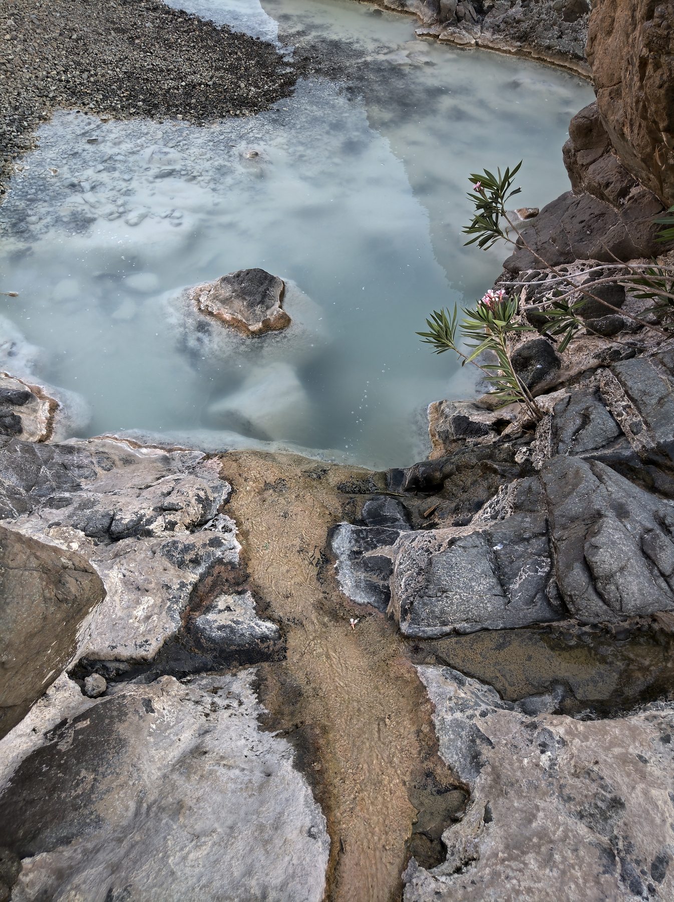 A milky-blue alkaline pool among dark ophiolite rocks